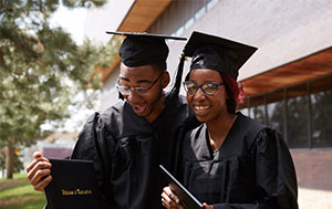 Students in graduation hats and gowns looking at their diplomas